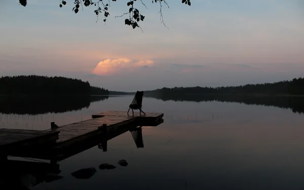 A solitary chair on a quiet dock at dusk, reflected in still water