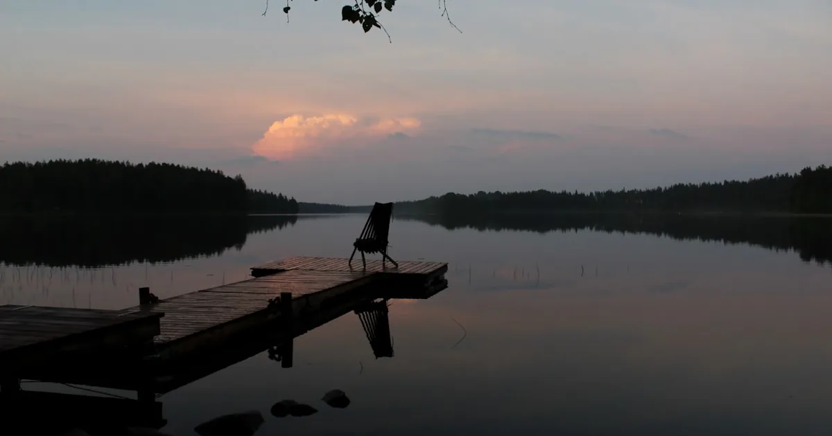 A solitary chair on a quiet dock at dusk, reflected in still water