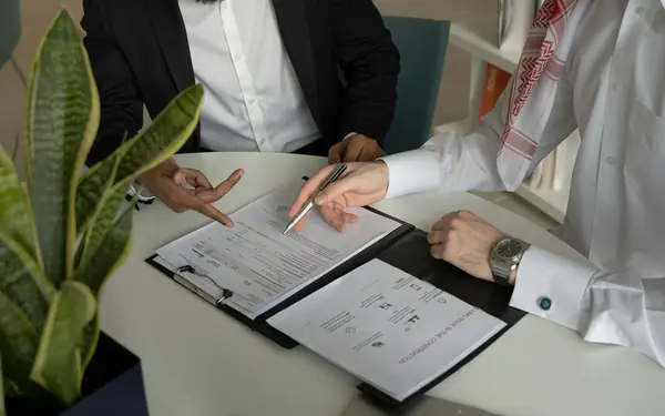 Two businessmen reviewing a signed contract at a desk, one wearing a keffiyeh