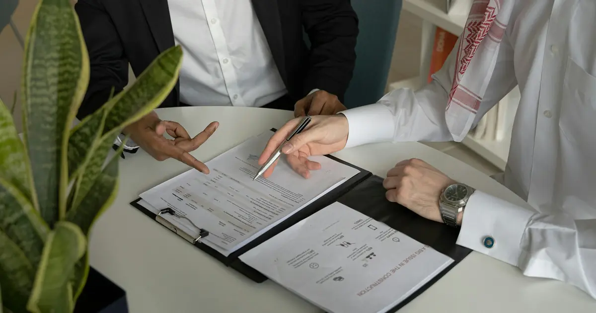 Two businessmen reviewing a signed contract at a desk, one wearing a keffiyeh