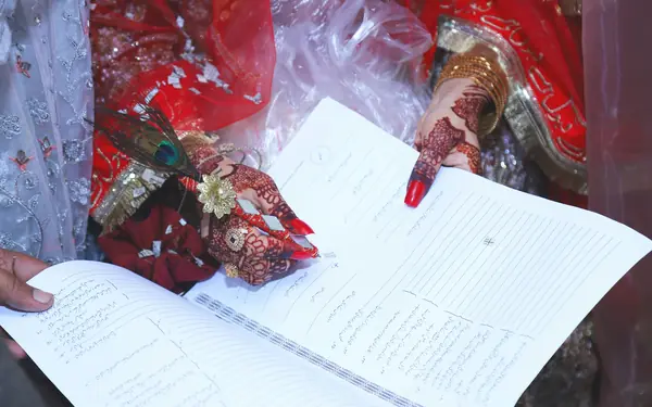 A bride's henna-decorated hand pointing to the Nikah Nama, the Islamic marriage contract document