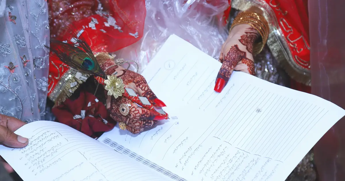 A bride's henna-decorated hand pointing to the Nikah Nama, the Islamic marriage contract document