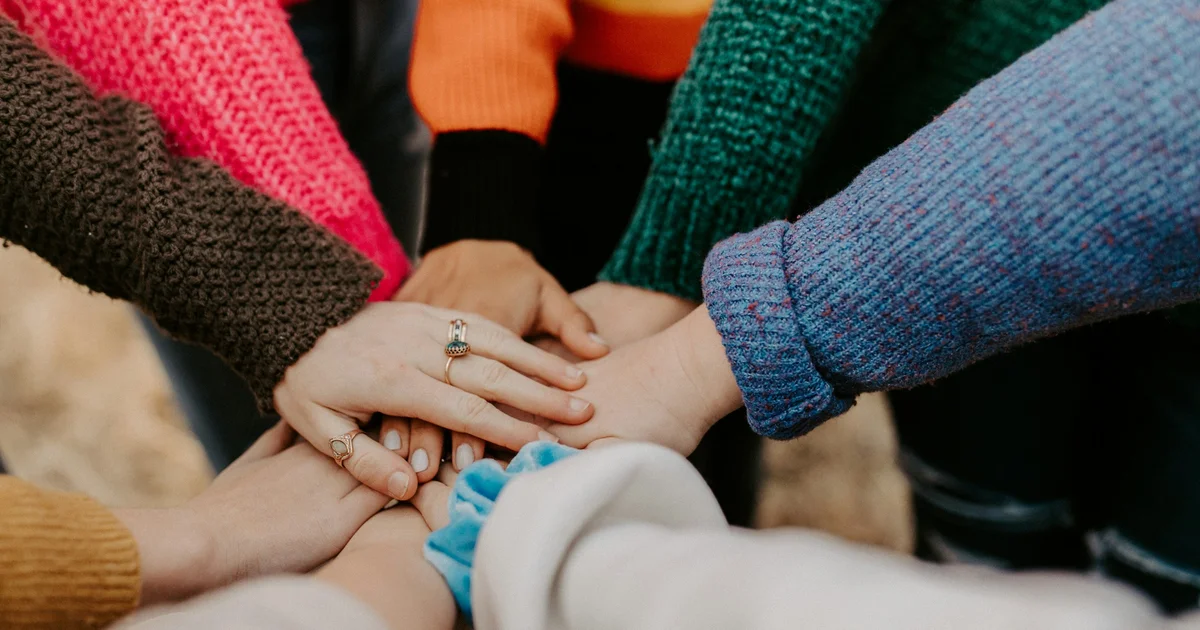 A group of people stacking their hands together in a circle, symbolising the mutual cooperation and shared responsibility at the heart of Takaful