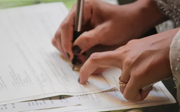 A hand wearing a ring signing an official document, representing the legal paperwork involved in Talaaq