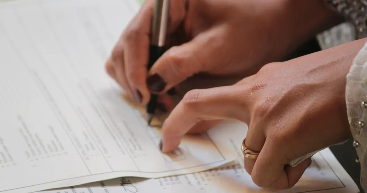 A hand wearing a ring signing an official document, representing the legal paperwork involved in Talaaq