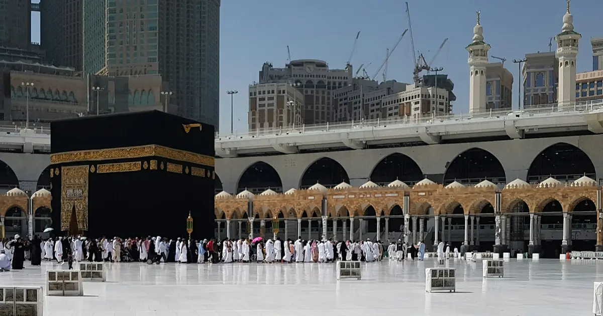 Pilgrims in Ihram and everyday dress walking near the Kaaba at Masjid al-Haram in Makkah